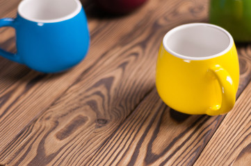 Four colored empty ceramic clean mugs on old worn brown wooden table