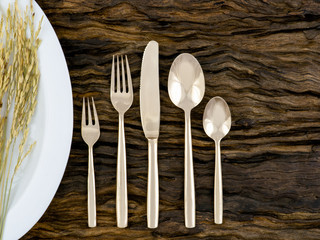 a set of five pieces of bronze cutlery, spoons, forks and knife with ear of rice on white plate on wooden plank