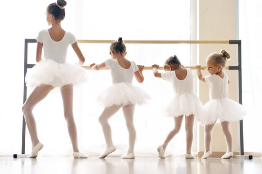 In a dance school, a group of girls and girls train together at the bar. all the little girls are dressed in white with gathered hair. Concept of: elegance, education, dance, learning