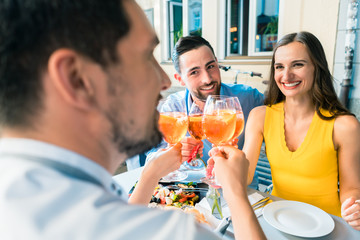 Two happy young couples with a trendy lifestyle toasting while sitting together at restaurant for a delicious lunch outdoors in summer