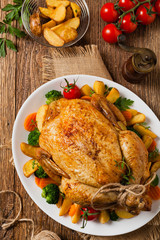 Roast chicken whole. Served on a plate with vegetables and baked potatoes.