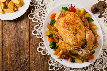 Roast chicken whole. Served on a plate with vegetables and baked potatoes.