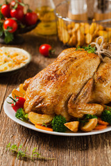 Roast chicken whole. Served on a plate with vegetables and baked potatoes.