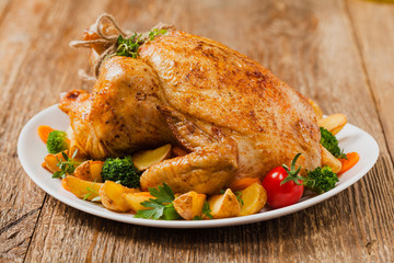 Roast chicken whole. Served on a plate with vegetables and baked potatoes.