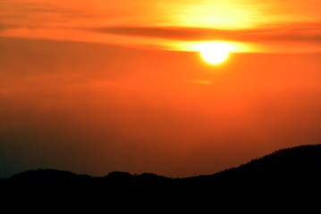 sunset sunrise in orange colors and sun over dark mountain silhouette.