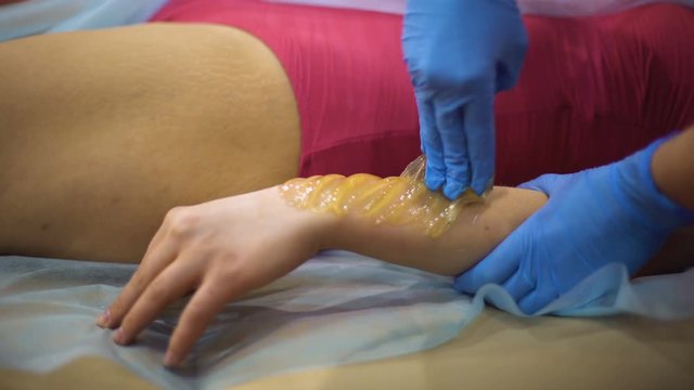 Beauty salon worker removing customer arms hair by sugaring paste, epilation