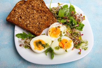Zdrowe śniadanie: Jajka gotowane na twardo, świeże kiełki, rukola i kromka pełnoziarnistego chleba  na niebieskim tle,  - obrazy, fototapety, plakaty