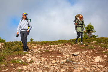 Travel Lifestyle and survival concept rear view. Hiking women  and men with backpack  enjoying the trekking, go to the mountains,  in the background a green field, mountains. 
