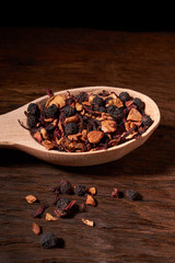 aromatic dry tea with fruits and petals in spoon, on wooden background. Concept of cosiness