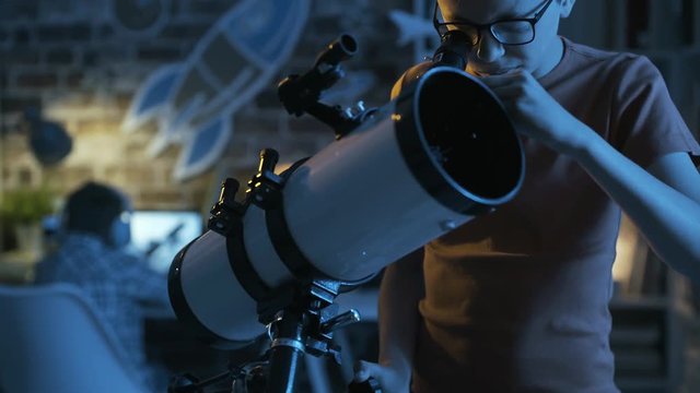 Smart young boy looking through a telescope at night