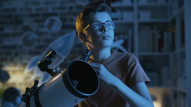 Smart young boy looking through a telescope at night