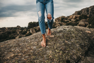 Crop barefoot woman in jeans walking on rock