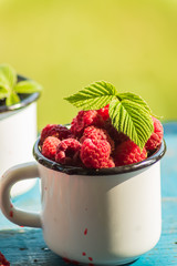 Ripe red raspberry in a emaned mug on old wooden table.