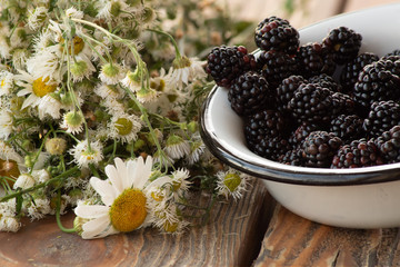 Ripe blackberry in an enamel  dish, and garden flowers, on old wooden table.