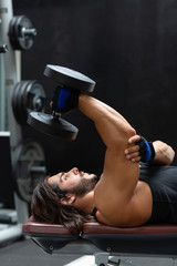 Fit strong man lifting a heavy dumbbell in a gym
