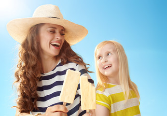 happy mother and child with ice cream on stick against blue sky