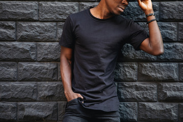 Man in blank black t-shirt standing against brick wall, cropped shot - obrazy, fototapety, plakaty