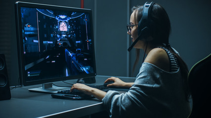 Beautiful Professional Gamer Girl Playing in First-Person Shooter Online Video Game on Her Personal Computer. Casual Cute Geek Girl Wearing Headset. In the Underground Gaming Club.