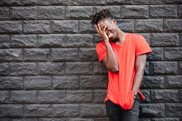 African man model laughing in red t-shirt against brick wall with facepalm