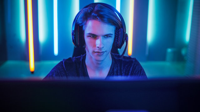 Portrait of the Young Pro Gamer Playing in Online Video Game, talks with Team Players through Microphone. Neon Colored Room. e-Sport Cyber Games Internet Championship.