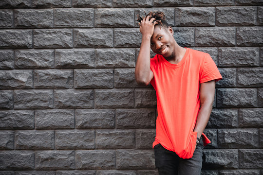 African man model smiling in red t-shirt against brick wall with facepalm