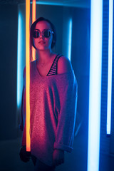 Portrait Shot of a Young Elegant Disco Girl Wearing Sunglasses. Room Lit in Retro / Retrowave Style with Neon and Pink Lights.