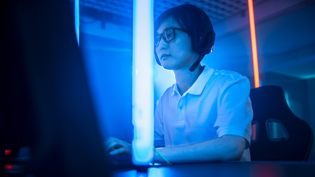 Low Angle Shot of a Professional East Asian Gamer Playing in Online Video Game on His Personal Computer. Room Lit by Neon Lights in Retro Arcade Style. Cyber Sport Championship.