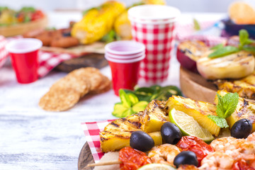 Picnic with grilled food. Sausages and corn on barbecue, shrimp, vegetables and fruits. Delicious summer lunch and plastic dishes. Top view