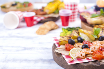 Picnic with grilled food. Sausages and corn on barbecue, shrimp, vegetables and fruits. Delicious summer lunch and plastic dishes. Top view