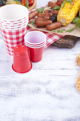 Picnic with grilled food. Sausages and corn on a barbecue. Delicious summer lunch and plastic dishes. Top view