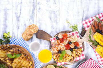 Picnic with grilled food. Sausages and corn on barbecue, shrimp, vegetables and fruits. Delicious summer lunch and plastic dishes. Top view