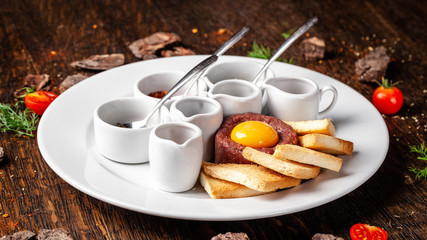 Tartare from raw beef meat with different spices and sauces separately for mixing. A glass of red wine on the table. Beautiful serve in the restaurant. Copy space, selective focus