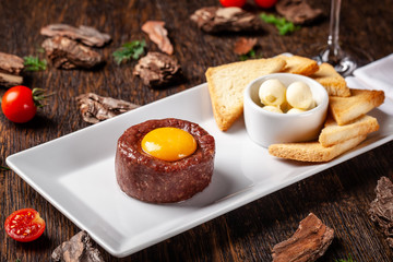 Tartare from raw beef meat with different spices and sauces separately for mixing. A glass of red wine on the table. Beautiful serve in the restaurant. Copy space, selective focus