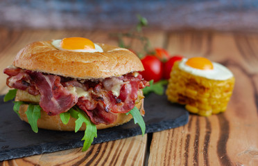 Bagel sandwich with turkey, bacon, ruccola, cheese, tomatoes ,corn and quail eggs .Bagel burger on the wooden background