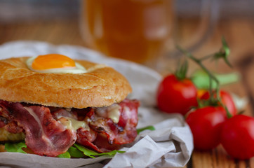 Bagel sandwich with turkey, bacon, ruccola, cheese, tomatoes and quail egg on the wooden background. Bagel burger with beer on the background
