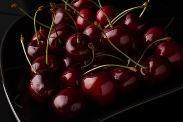 Bowl of cherries on a black background. Dark image of red cherries on a black reflective surface.