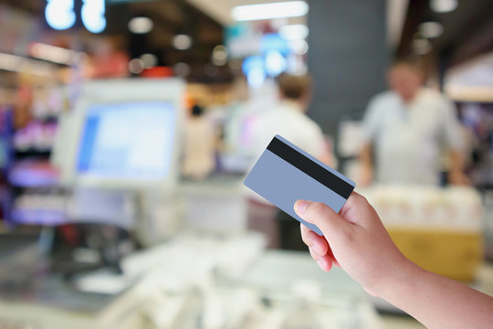 Hand Hold Credit Card With Supermarket Cashier Checkout Counter With Customer Defocused Blur Background