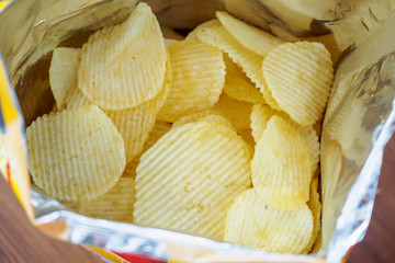 Potato chips in open snack bag close up on table floor