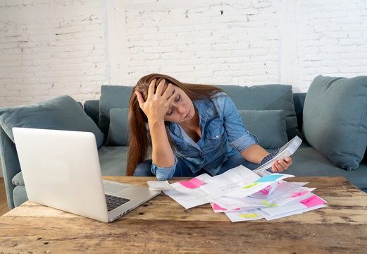 Portrait of worried young single mother feeling stressed while working through finances with laptop and calculator in living room in paying off debts and domestic bills and financial problems concept.
