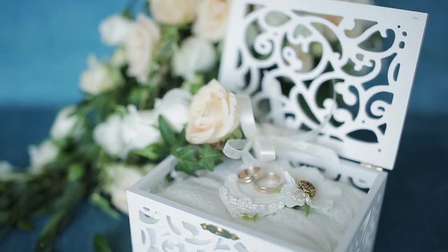 Wedding concept. Wedding rings in a wooden box handmade, surrounded by flowers on a turquoise background.
