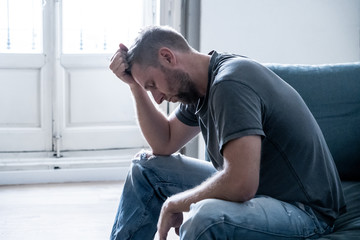 Unhappy depressed caucasian male sitting and lying in living room couch feeling desperate a lonely. In stressed from work, anxiety, heartbroken and depression concept