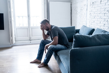 Unhappy depressed caucasian male sitting and lying in living room couch feeling desperate a lonely. In stressed from work, anxiety, heartbroken and depression concept