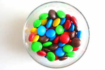 colorful button-shaped candies coated chocolate sweets in glass bottle on white background, in glass jar