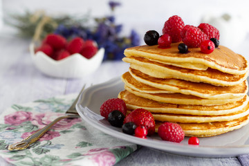 Stack of gold pancakes with berries and honey on wooden background