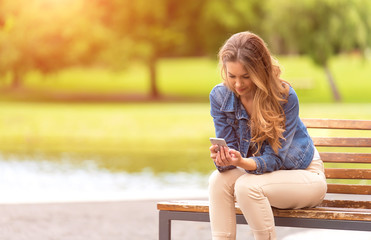 Young woman sitting on bench and use her phone in park
