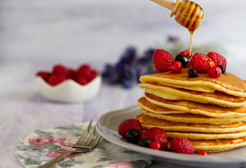 Stack of gold pancakes with berries and honey on wooden background.Honey dripping from dipper on pancakes. life style