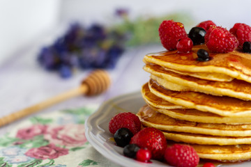 Stack of gold pancakes with berries and honey on wooden background