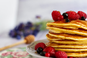 Stack of gold pancakes with berries and honey on wooden background