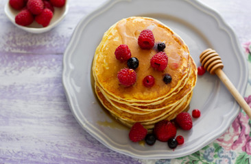 Stack of gold pancakes with berries and honey on wooden background. Top view