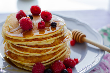 Stack of gold pancakes with berries and honey on wooden background